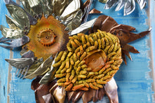 Load image into Gallery viewer, Detail of Sunflowers III by Scoobafish, showing two sculptural sunflower heads made from recycled metal, rusted components and copper-toned leaves on a blue painted panel.