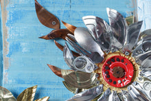 Load image into Gallery viewer, Close-up detail of Sunflowers III by Scoobafish, featuring a silver recycled-metal sunflower with a red mechanical centre and copper-toned leaves on a blue painted background.
